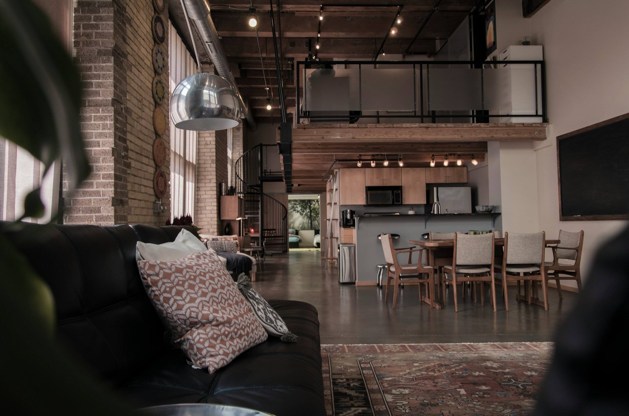 Loft en brique avec mezzanine bordée d’un garde-corps métallique noir et escalier hélicoïdal